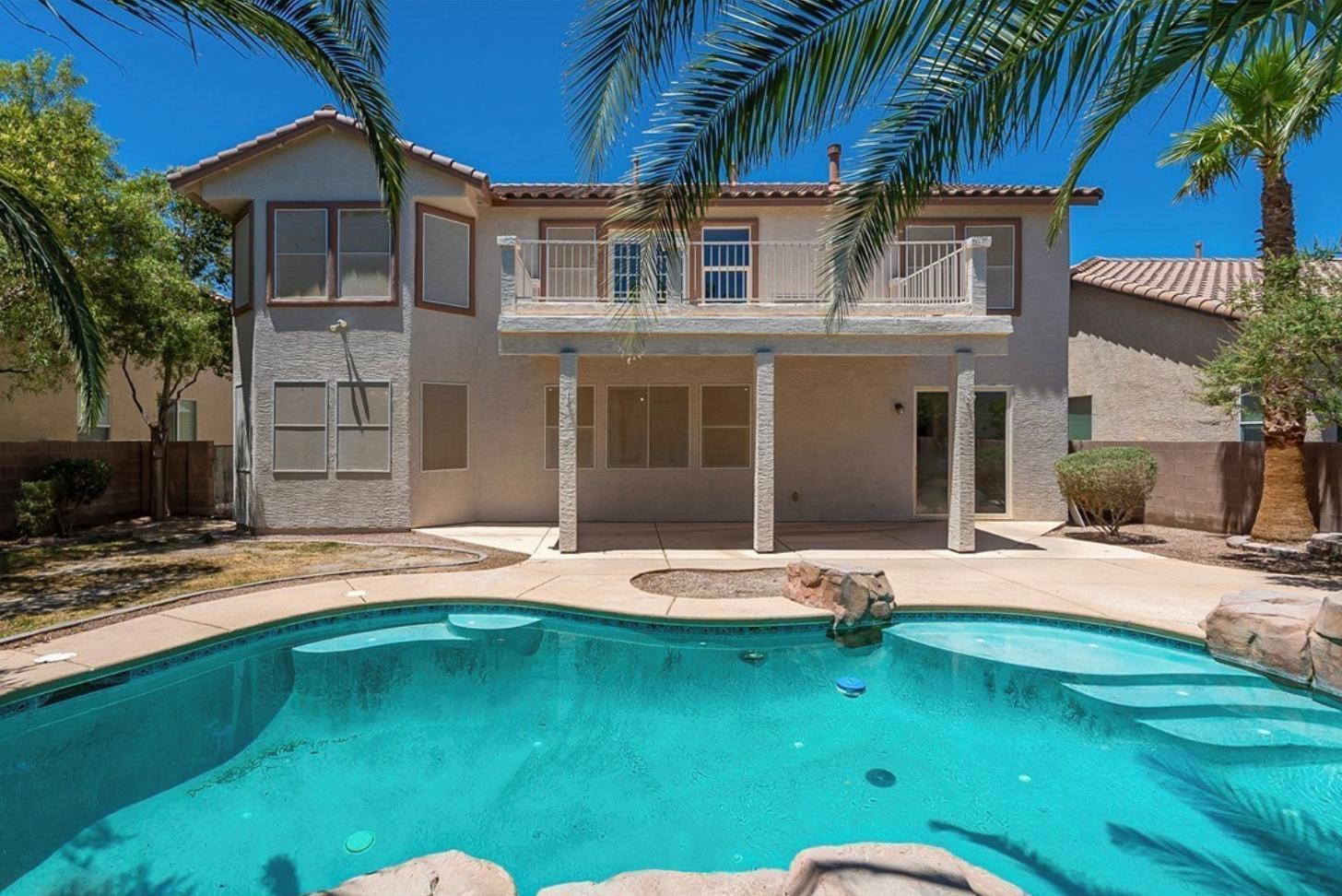 A two story home with a large balcony, covered patio, and resort-style pool area with palm trees